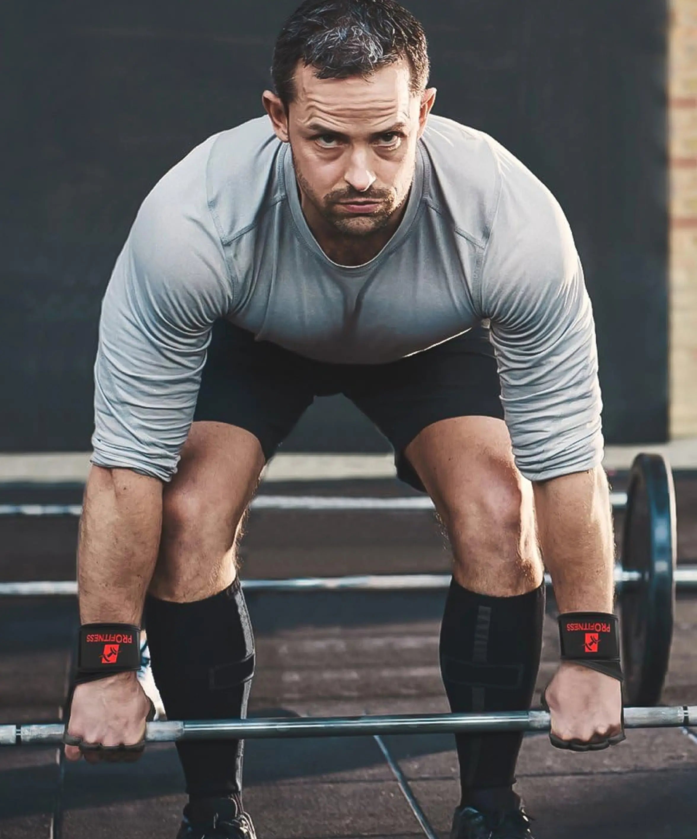 A man lifting a barbell in a gym, wearing wrist wraps and athletic gear.